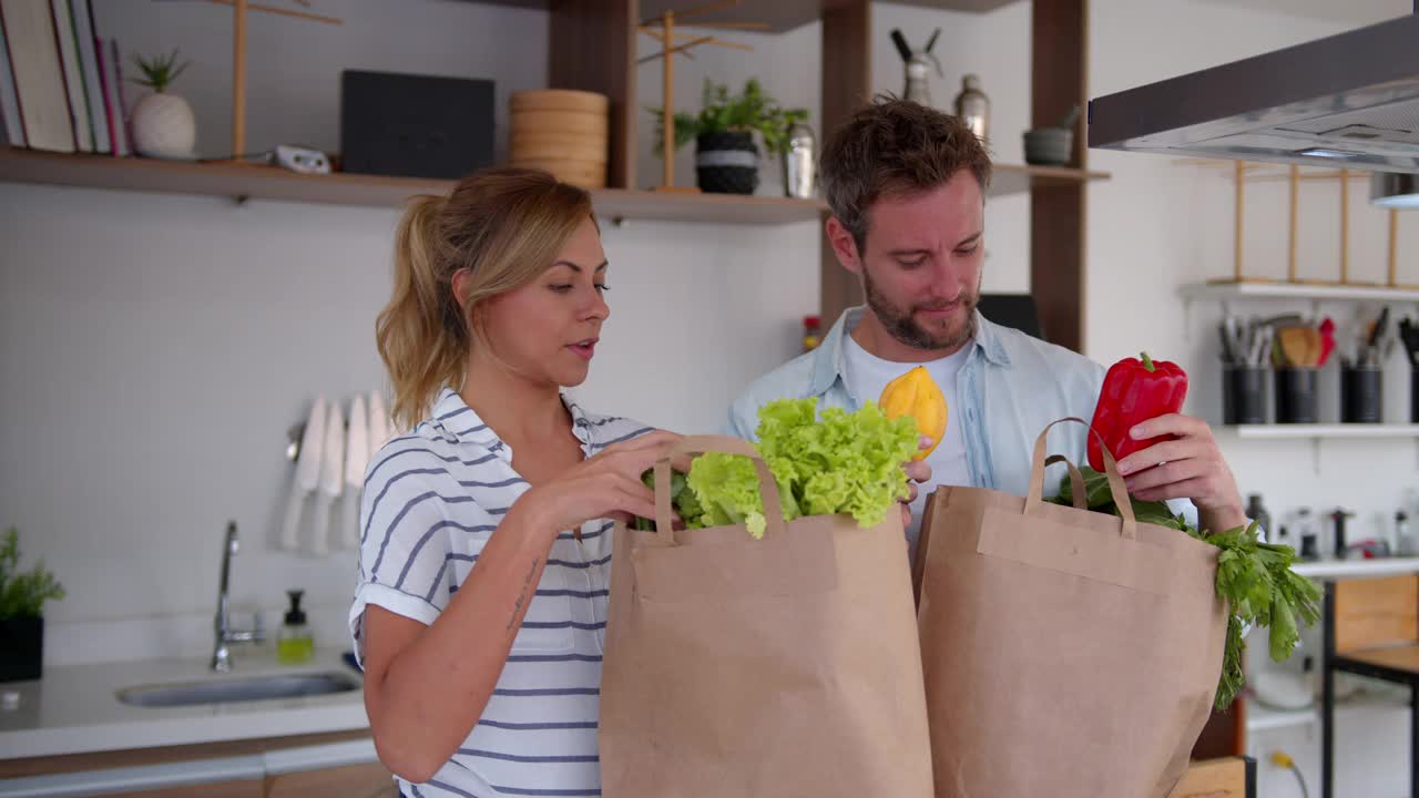 幸福的年轻夫妇在他们的厨房柜台边聊天边打开食品杂货快递视频素材