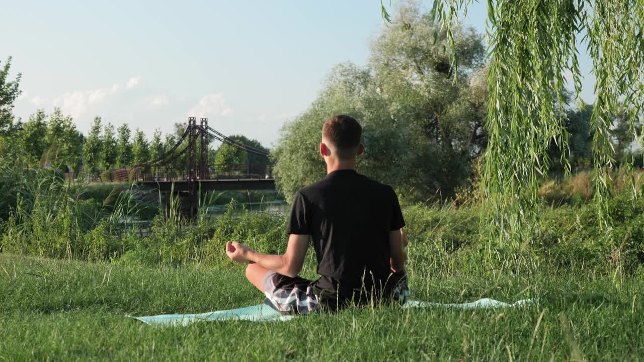 后视图的年轻人坐在瑜伽垫莲花位和冥想在城市公园。男人们在阳光明媚的户外练习瑜伽。瑜伽的清晨功课视频素材