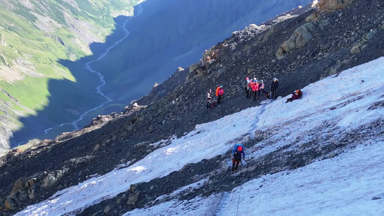 一名戴着红色头盔的登山者沿着冰碛石行走，用登山杆沿着带保护绳的绳子移动视频素材