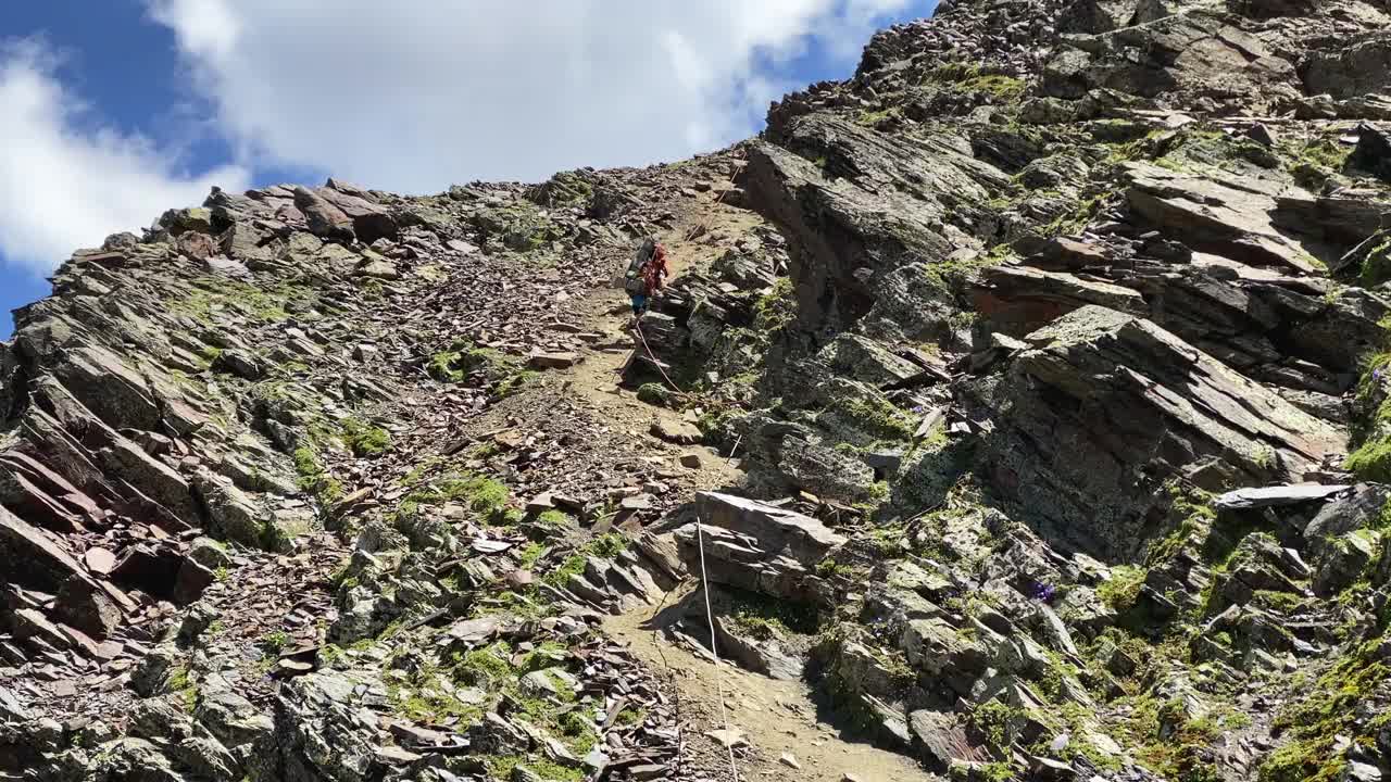 一个徒步旅行者背着大背包沿着山路走下悬崖，手里抓着一根绳子视频素材