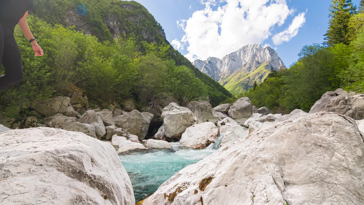 一个年轻女子穿过山河，从一块岩石跳到另一块岩石。风景如画的风景视频素材