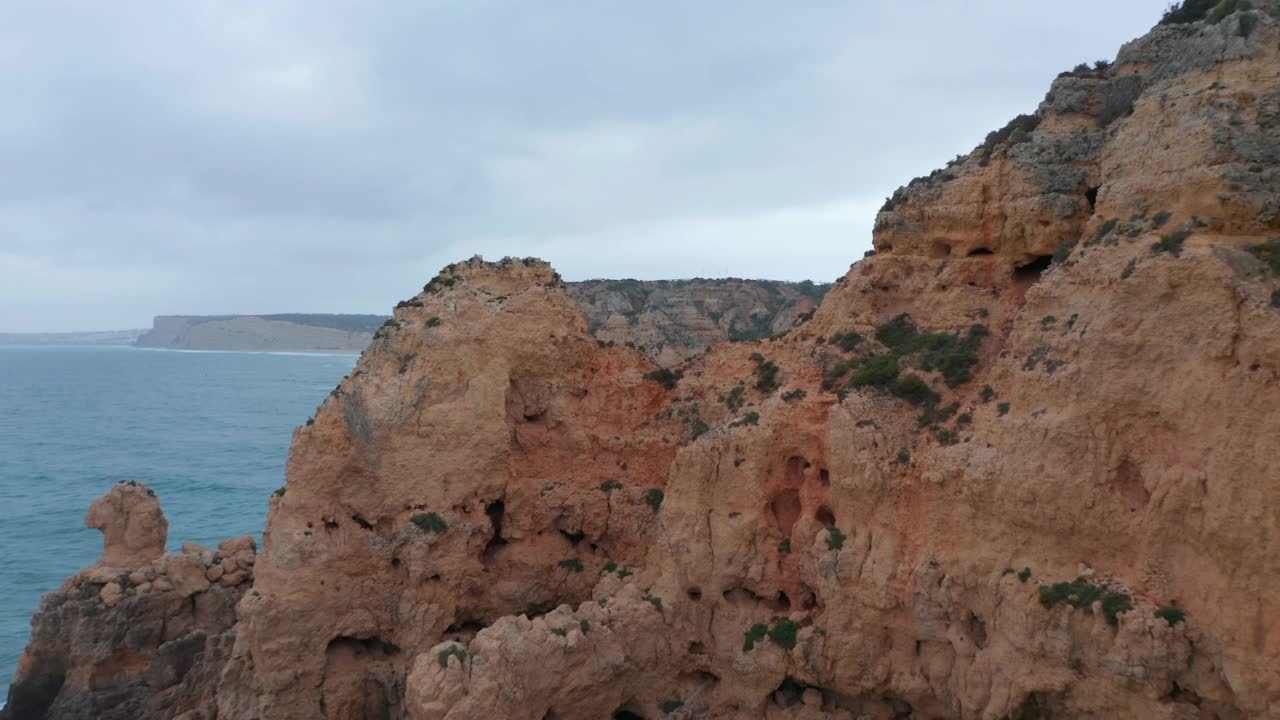 拉各斯惊人的岩石悬崖海岸线的鸟瞰图，无人机在海岸上飞行揭示惊人的背景海景，阴天视频素材