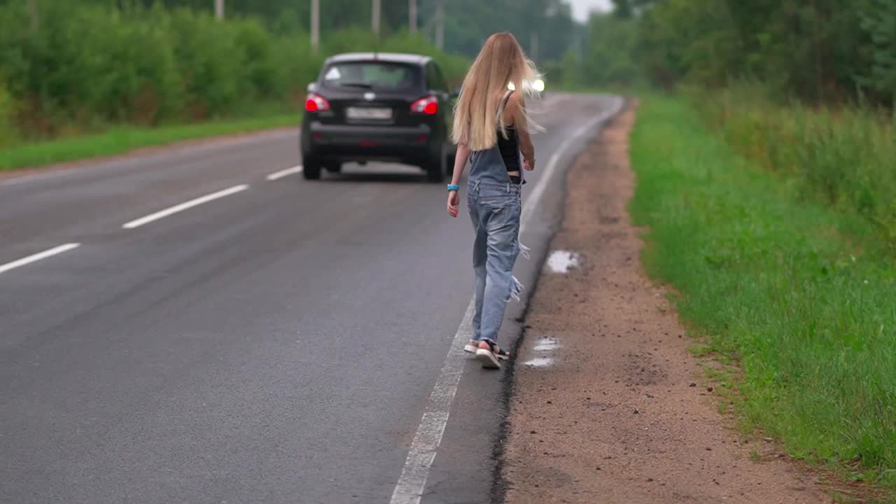 一个女孩在高速公路上走着，试图拦住一辆过路的汽车视频下载