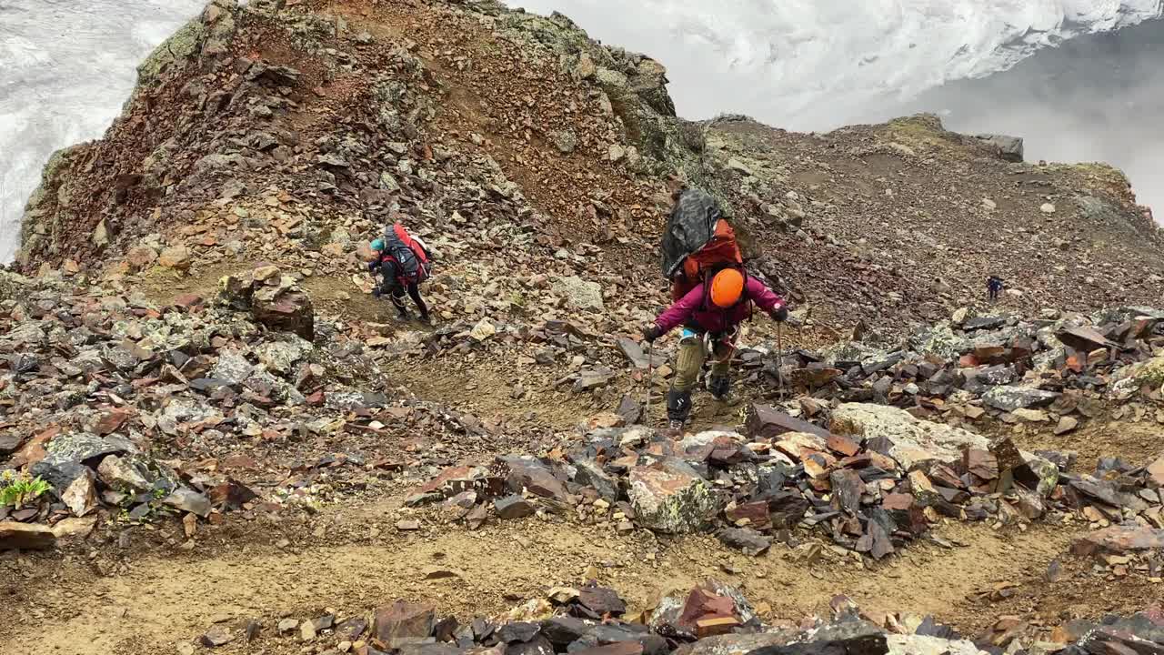 一个疲惫的游客背着一个大背包，跌跌撞撞地沿着山路，经过巨石视频素材