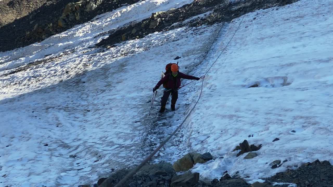 一名登山者沿着冰碛走着，手里抓着一根有保护绳的绳子视频素材