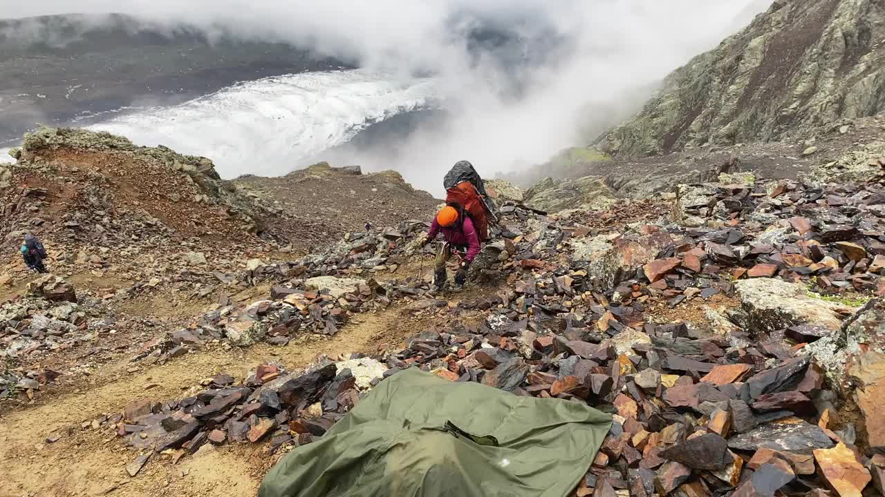 一个筋疲力尽的游客背着一个大背包，跌跌撞撞地沿着山路，经过巨石视频素材