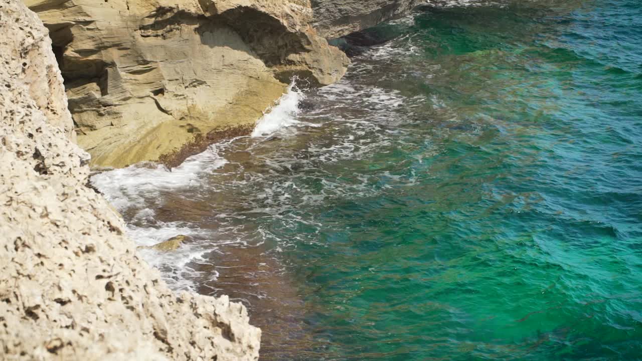 阳光明媚的一天，小波浪拍打着岩石海岸，从上面看，慢动作视频视频素材