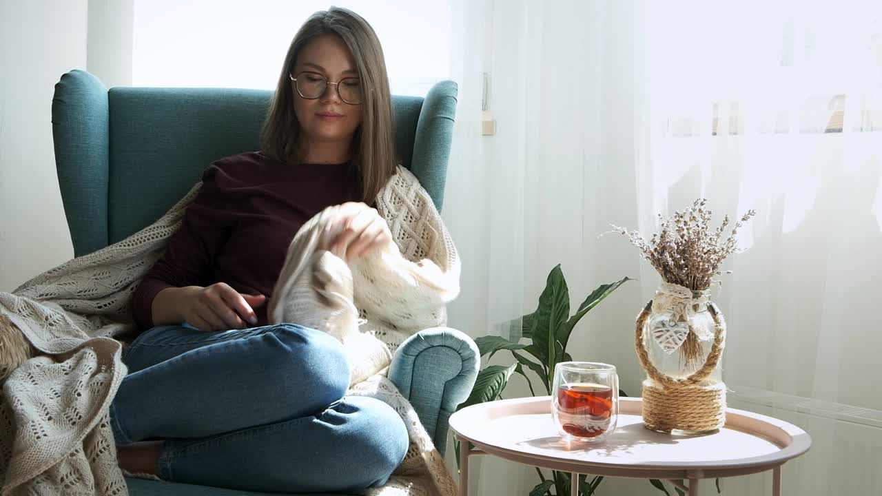 年轻的女人戴着眼镜，罩着舒适的格子呢，坐在舒适的扶手椅里睡觉视频素材