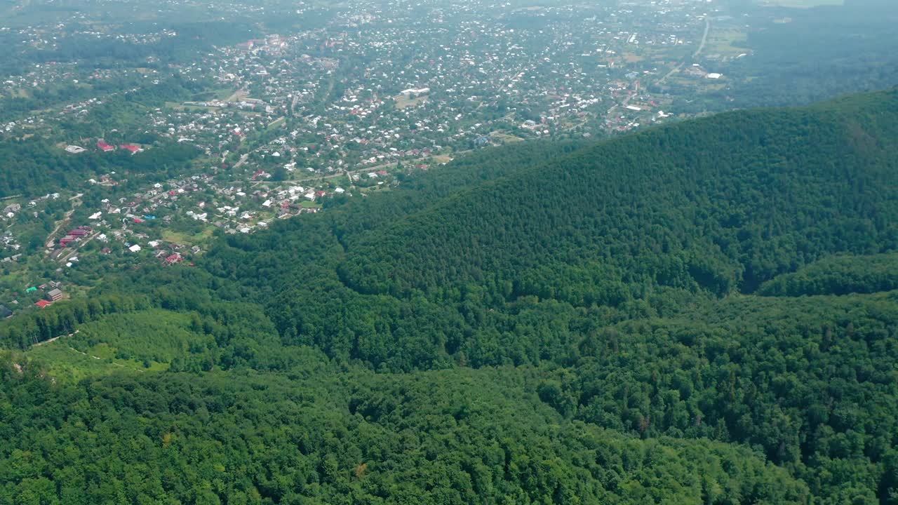 鸟瞰图中的村庄位于山谷后面，山上覆盖着茂密的绿色森林。视频素材