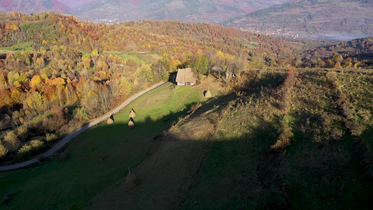 在罗马尼亚特兰西瓦尼亚，空中飞过秋天的乡村山景，有木屋、茅草屋顶和土路视频素材