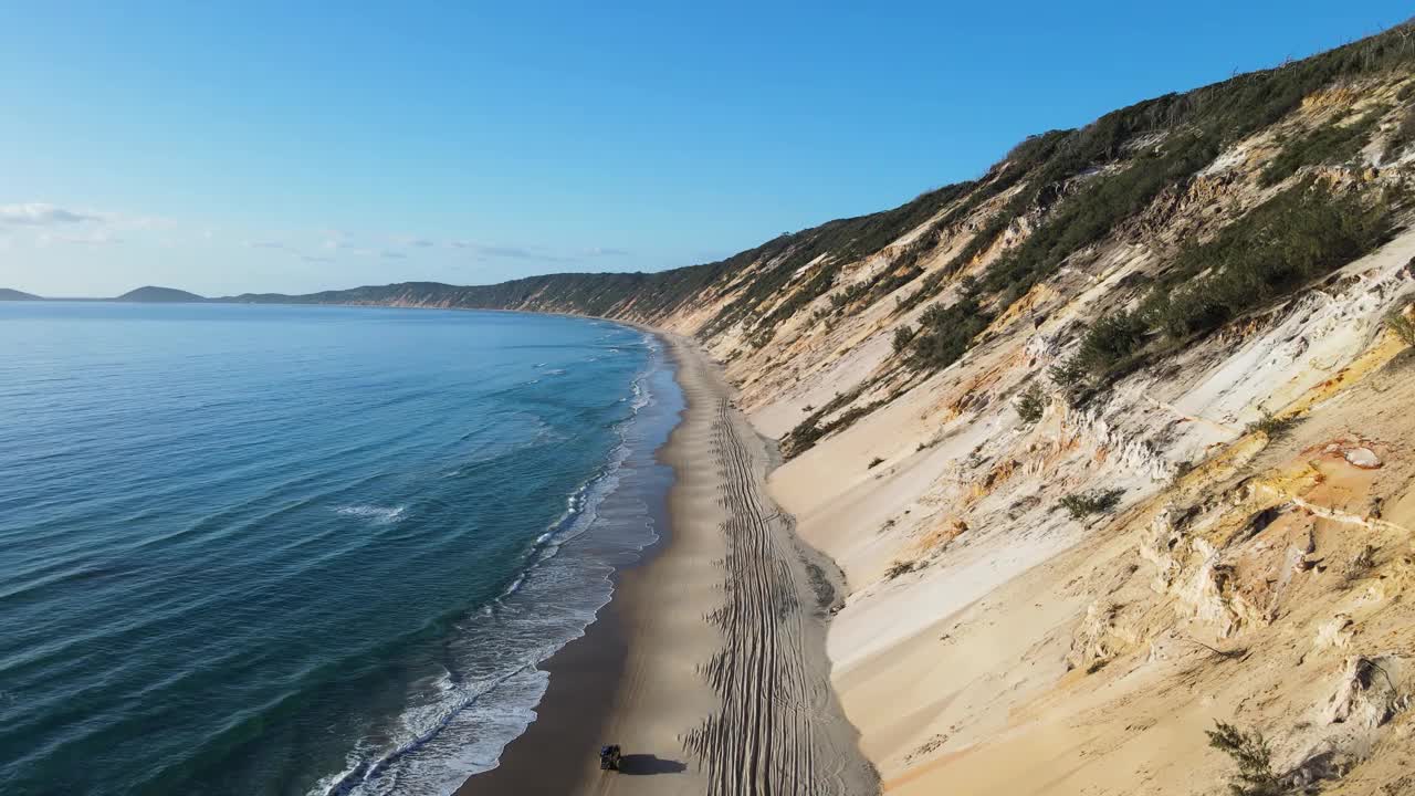 四驱车行驶在海浪和陡峭的沙崖之间的荒芜的海岸线海滩道路。视频素材