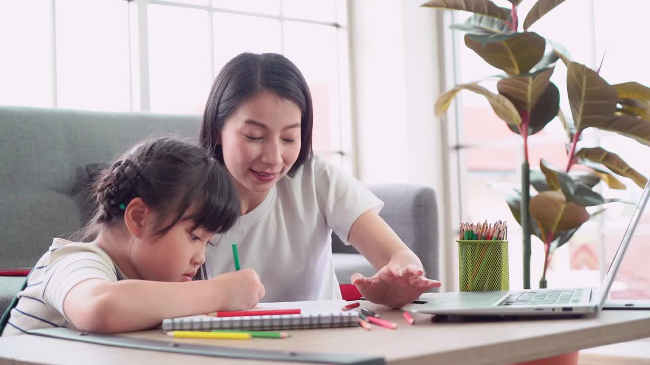 妈妈正在帮助女儿做家庭作业和涂色本，以进行艺术教育和创作活动。视频素材