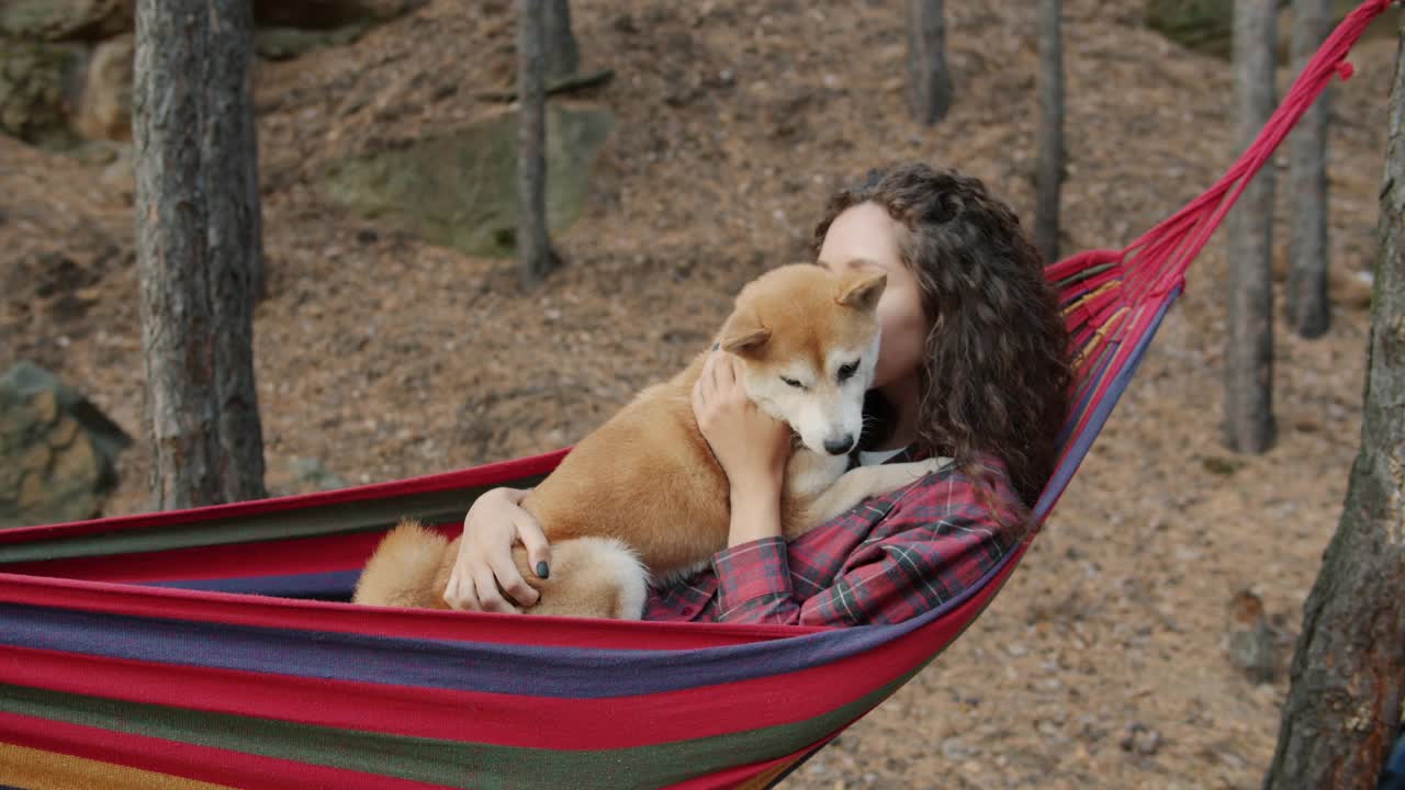 可爱的女孩在吊床上休息，柴犬在秋天的森林里度过休闲时光视频素材