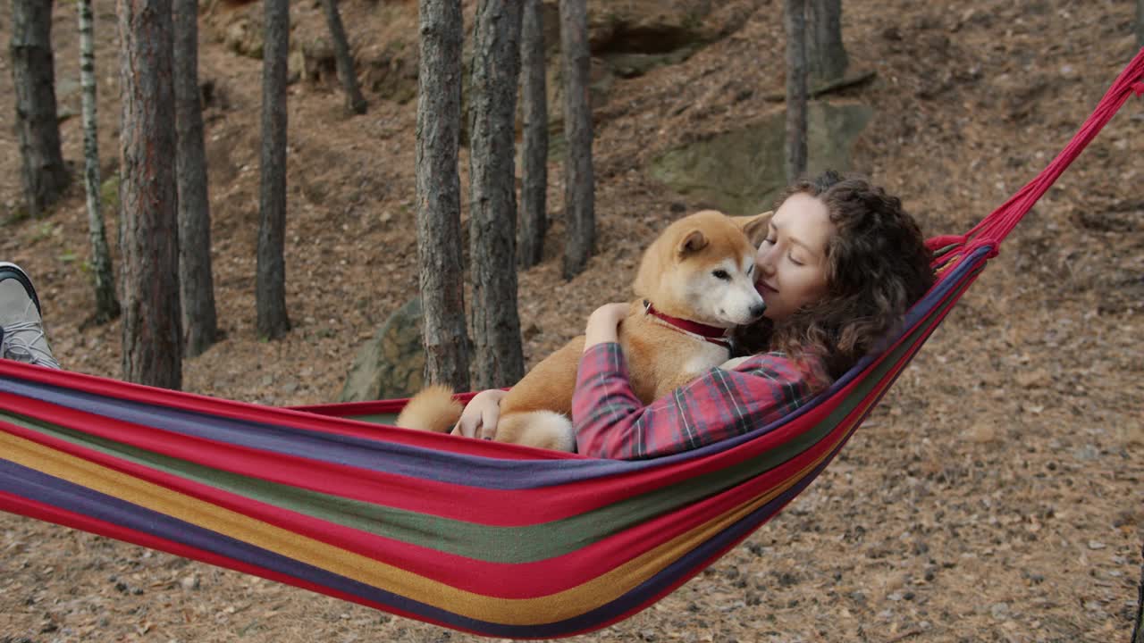 美丽的年轻女子的肖像在秋天森林的吊床上亲吻柴犬视频素材