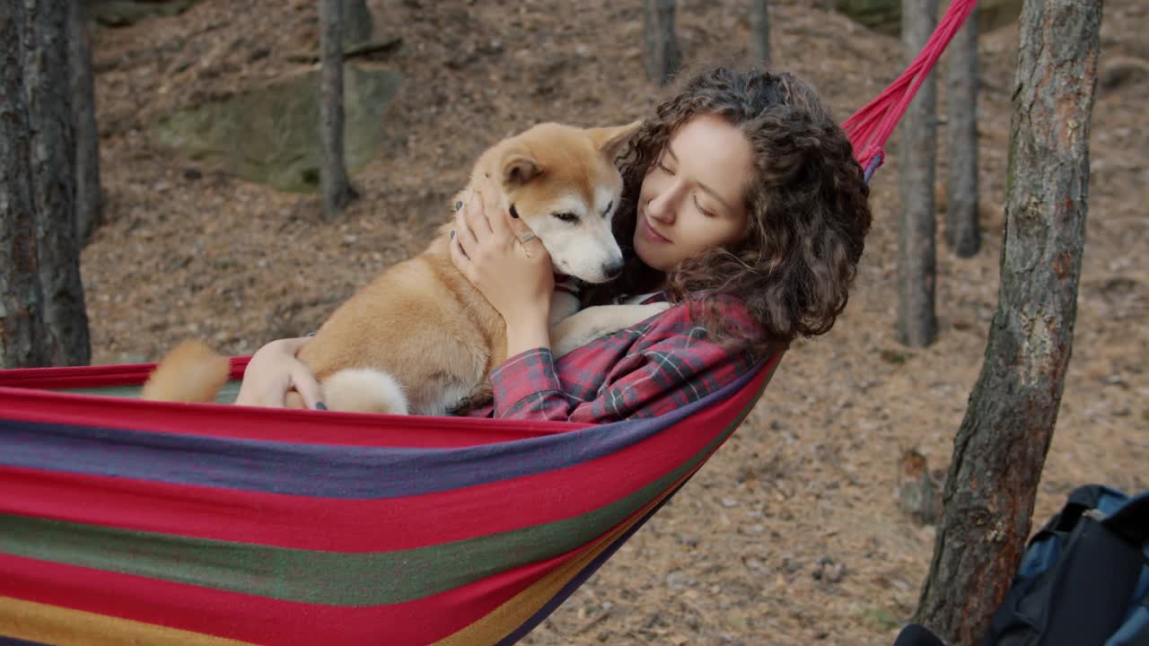 秋天的一天，美丽的年轻女士抱着可爱的柴犬在森林的吊床上荡秋千视频素材