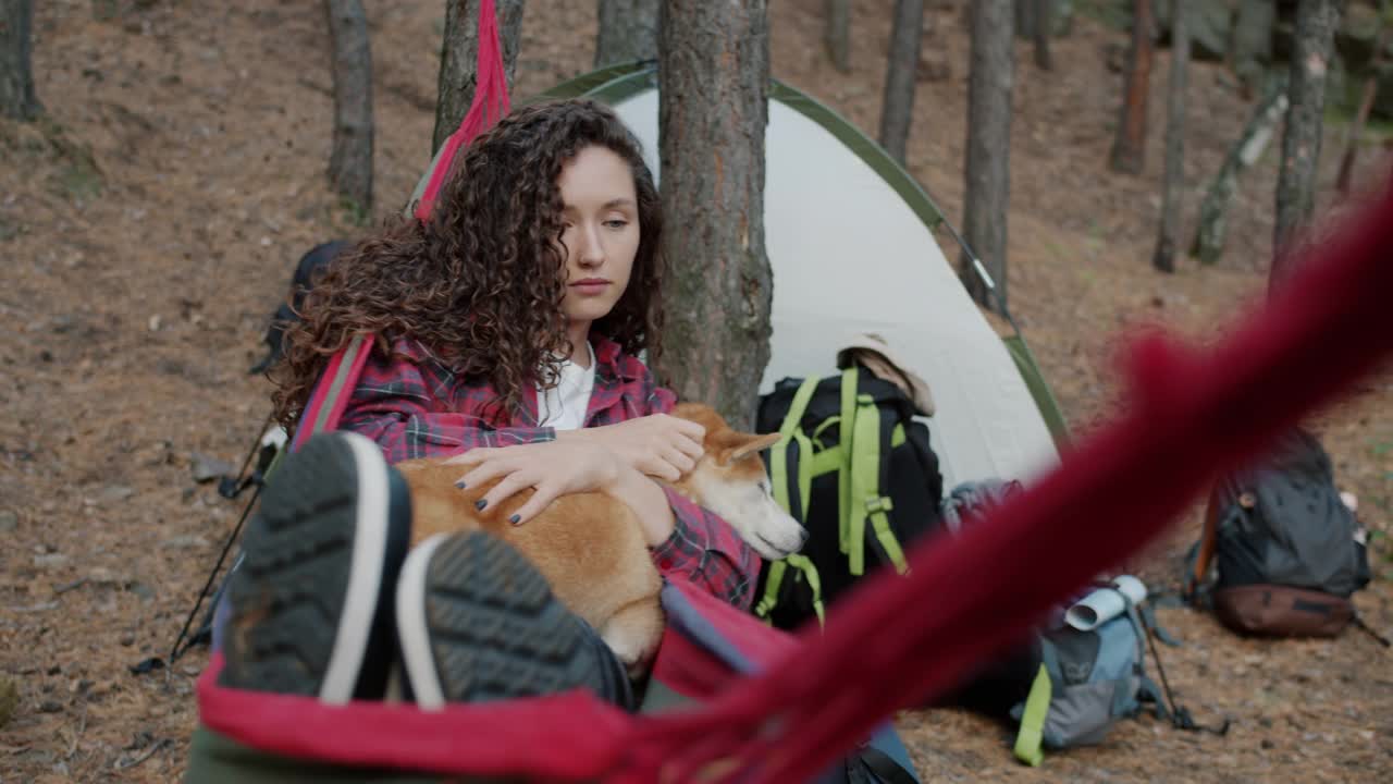 快乐的女游客在吊床上放松，抚摸可爱的柴犬，享受秋天森林的宁静视频素材