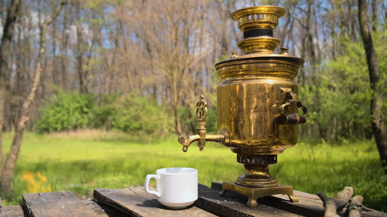 带烟的烧木头的古董茶炊。一位游客把茶炊里的水倒进杯子里。视频素材