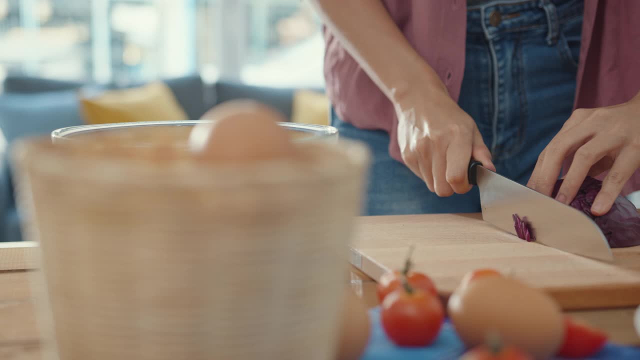 年轻的亚洲女厨师手握刀把大白菜切在屋内的餐桌木板上。视频素材