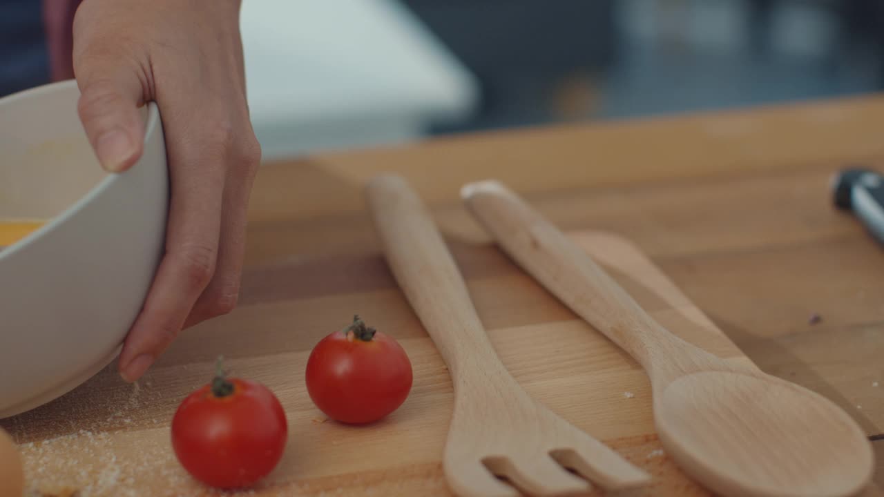 年轻的亚洲女厨师把鸡蛋搅拌到陶瓷碗里，在厨房桌子上的木板上用蔬菜做煎蛋卷。视频素材