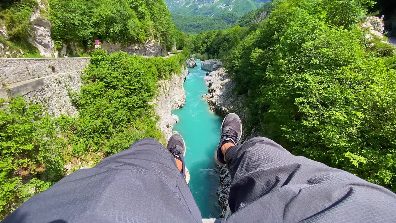 一个人坐在山涧上的桥上，双脚摇晃着视频素材