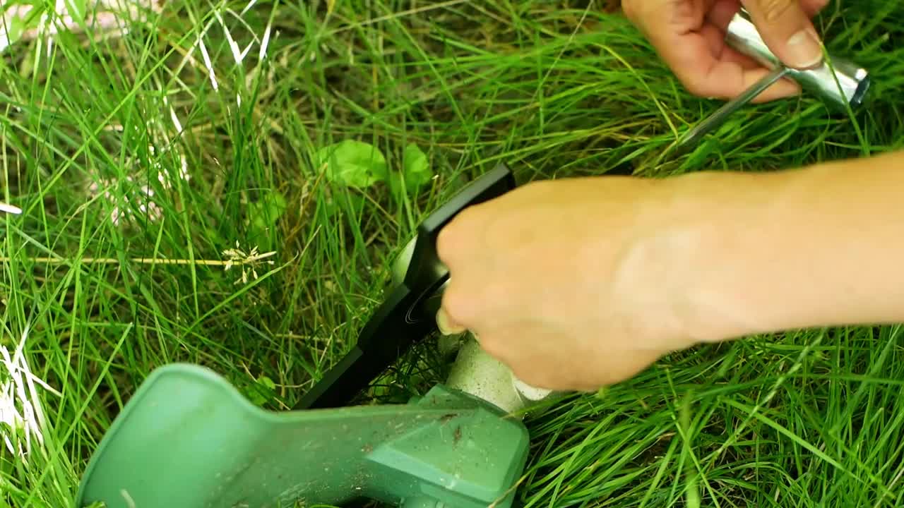 一名男子在外面割草前把刀放在割草机上。一个男人的手，组装和清洁。草机视频素材