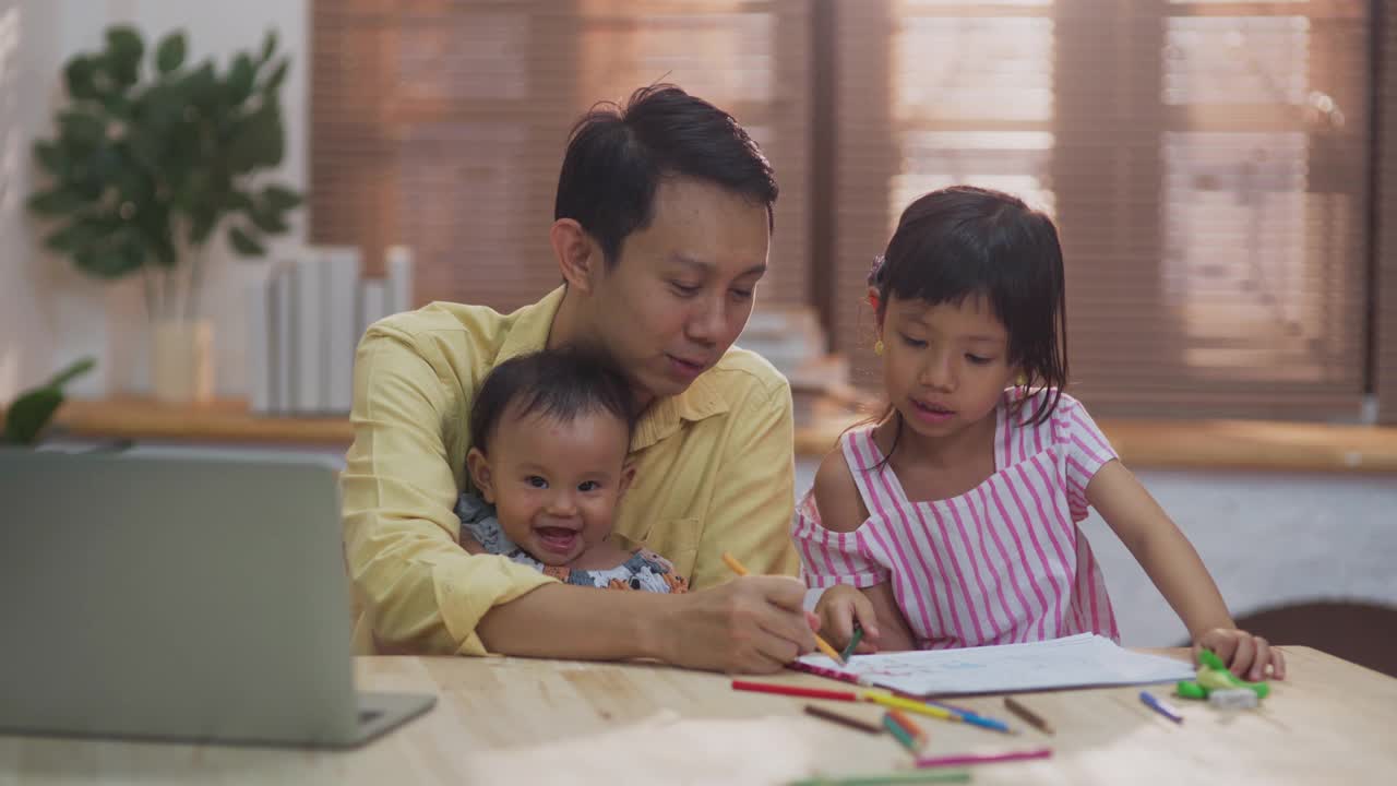 一个年轻人一边用笔记本电脑在家工作，一边帮助和教一个女孩做作业视频素材