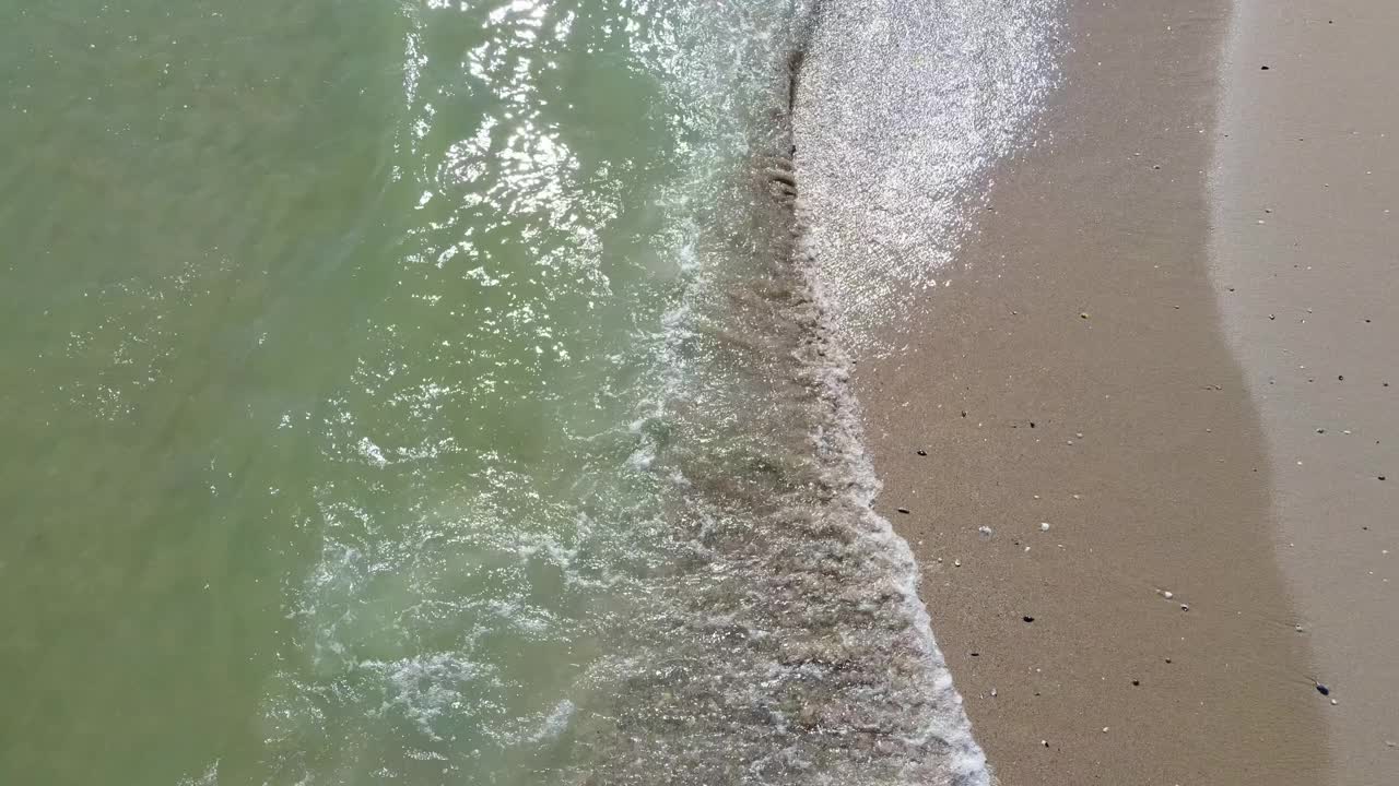 无人机在黑影上方飞得很高。鸟瞰图在暴风雨的海或海洋与美丽的波浪图案在沙滩上。夏日里无尽的海蓝宝石般的海水景观。视频素材