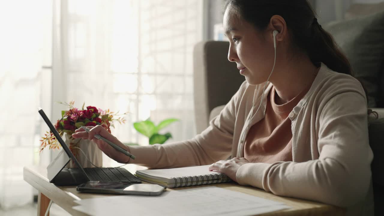 亚洲妇女戴着耳机和她的老师学习在笔记本电脑屏幕上在线家庭学校在线学习视频素材