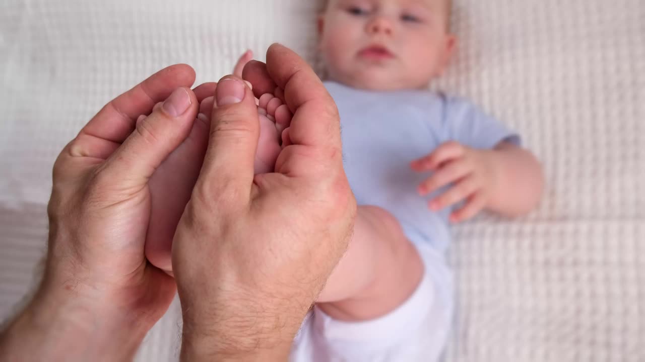 爸爸抱着宝宝的脚。新生儿在男性父母手上。孩子们的脚在父亲的掌心。特写镜头。孩子的小脚趾和幸福父母的大人的手。父亲节的节日。视频素材