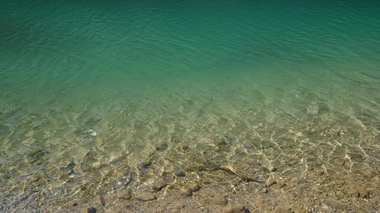 清澈的河水在波纹的梯度下，水底有岩石。阳光照射在水面上视频下载