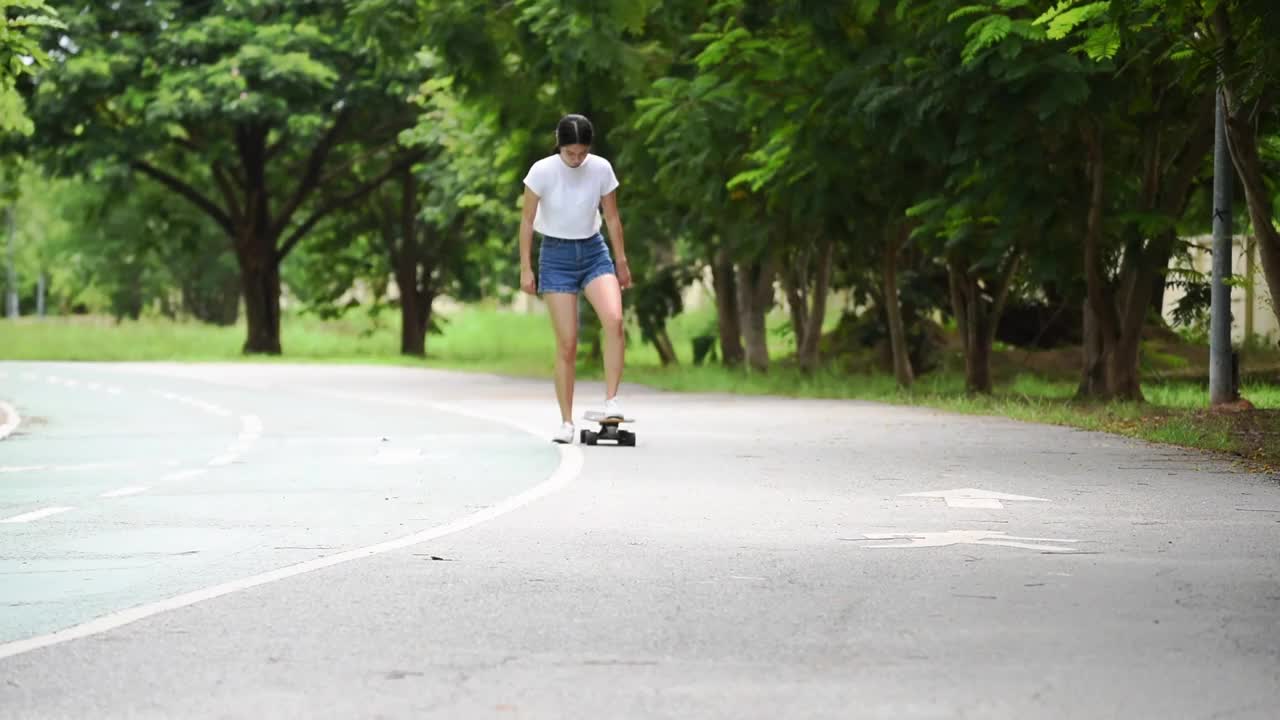 女孩在牛仔短裤，摆姿势在夏天与五颜六色的滑板长板。生活方式的概念视频下载