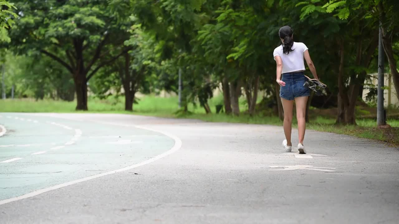 女孩在牛仔短裤，摆姿势在夏天与五颜六色的滑板长板。生活方式的概念视频素材