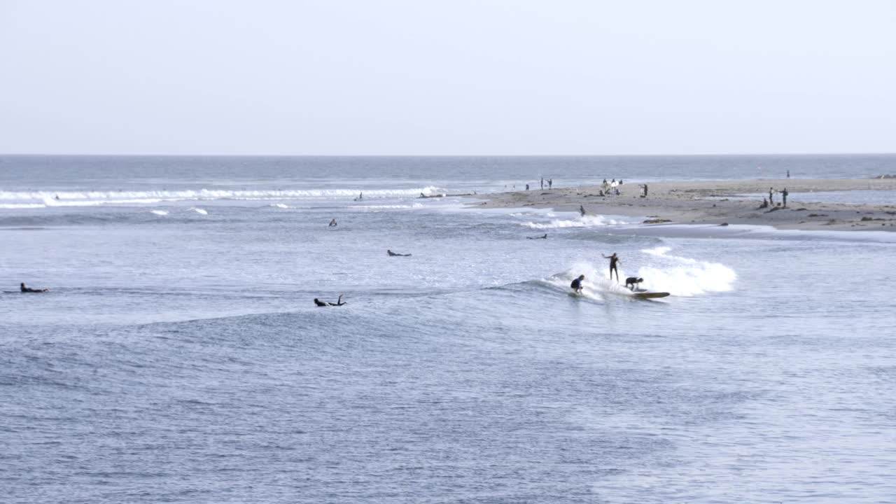 中等角度的冲浪者在海湾或海洋冲浪。在bg中可以看到海滩、海岸、人群和救生员塔。视频素材