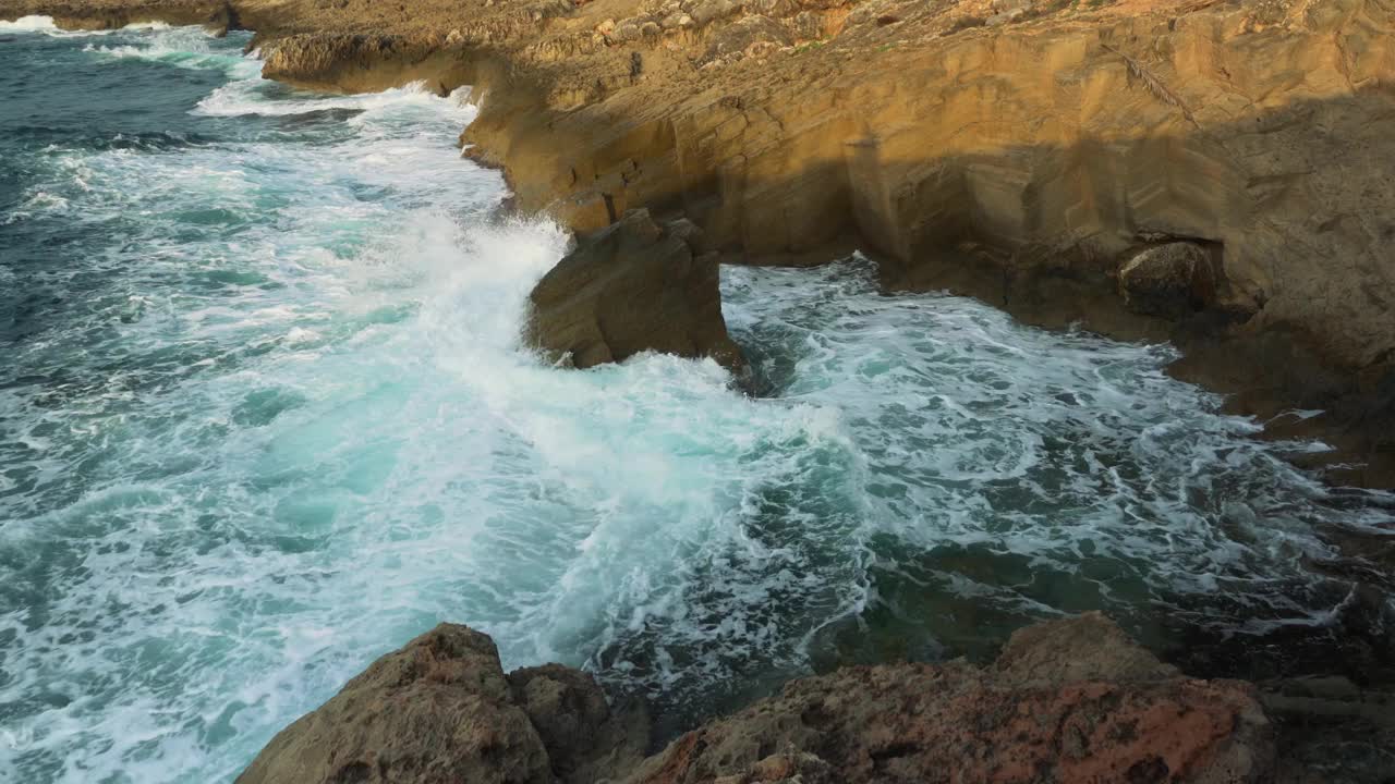 阳光明媚的日子里，小波浪拍打着岩石海岸，从上面往下看视频素材