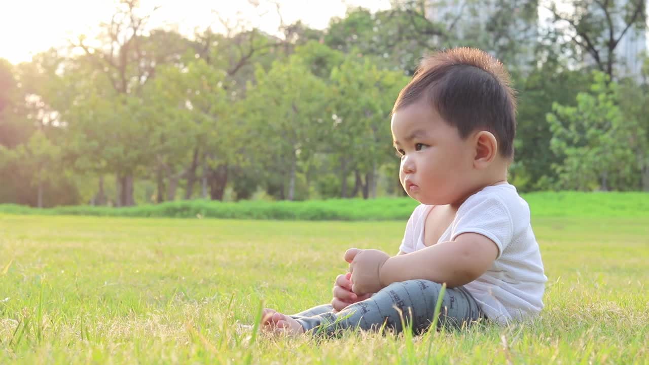 快乐可爱可爱的婴儿蹒跚学步坐在草坪上。视频素材