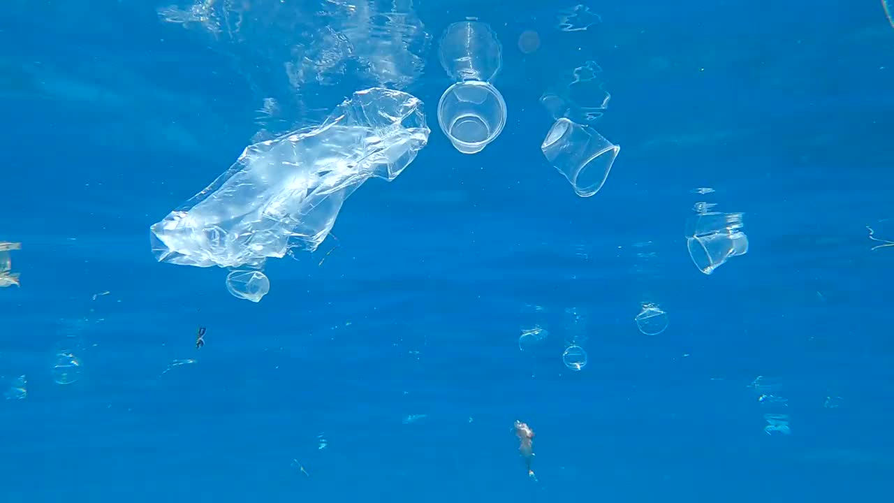 许多塑料垃圾漂浮在水面上，被阳光反射到水面上。水下拍摄，海洋塑料污染。红海的大量塑料污染(4K - 60fps)视频素材