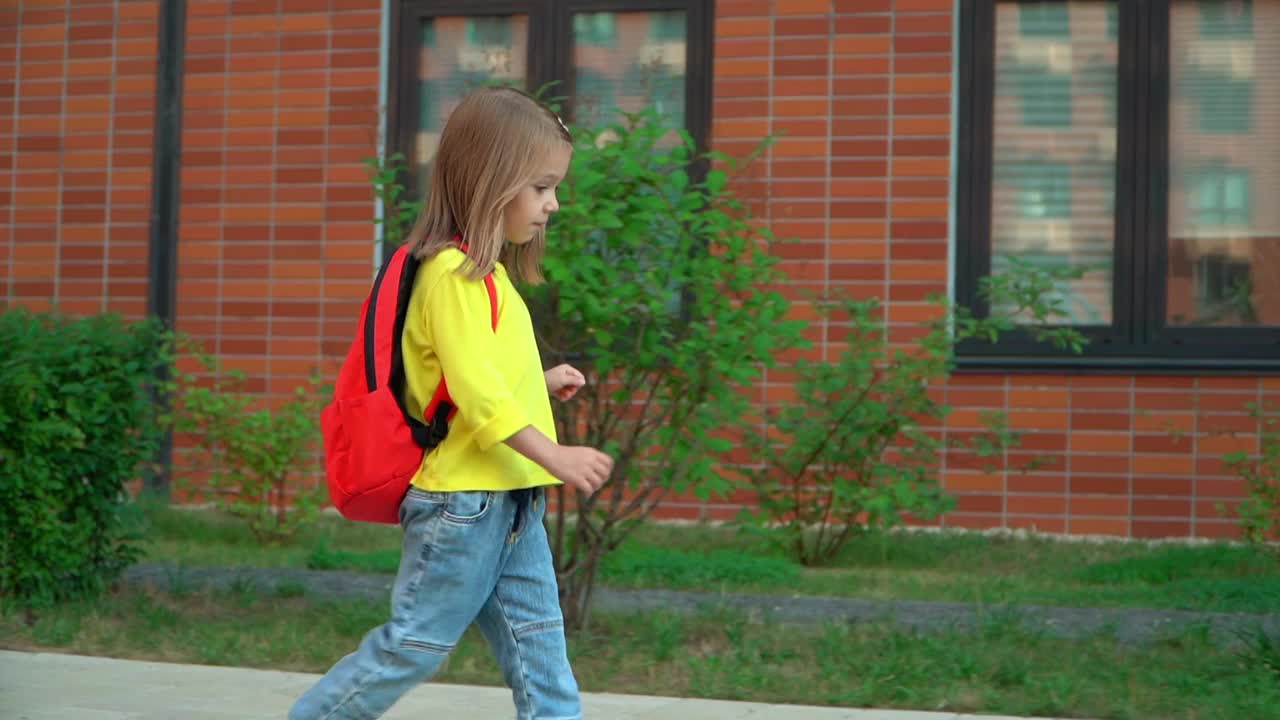 学校。小女孩背着书包在校园里又跑又跳。快乐的小学生在户外玩耍。教育和学前概念。视频素材