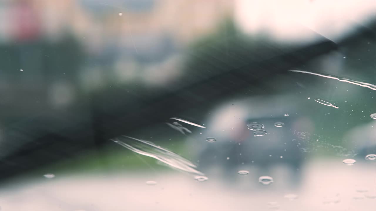 雨滴落在汽车挡风玻璃上，雨刷把它们冲洗掉。视频素材