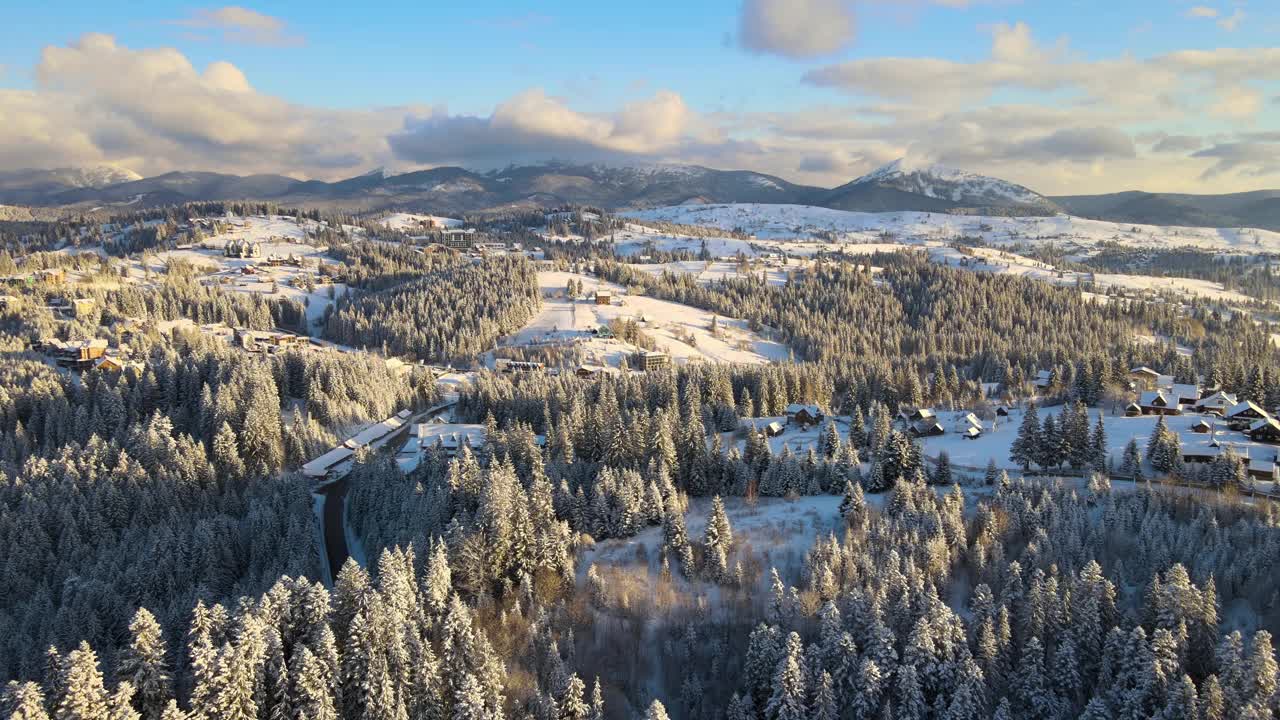 空中冬季景观与小村庄房屋之间的雪覆盖森林在寒冷的山在晚上。视频素材