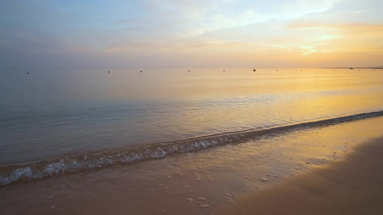 日出时，沙滩上平静的海岸与破碎的海浪。视频素材