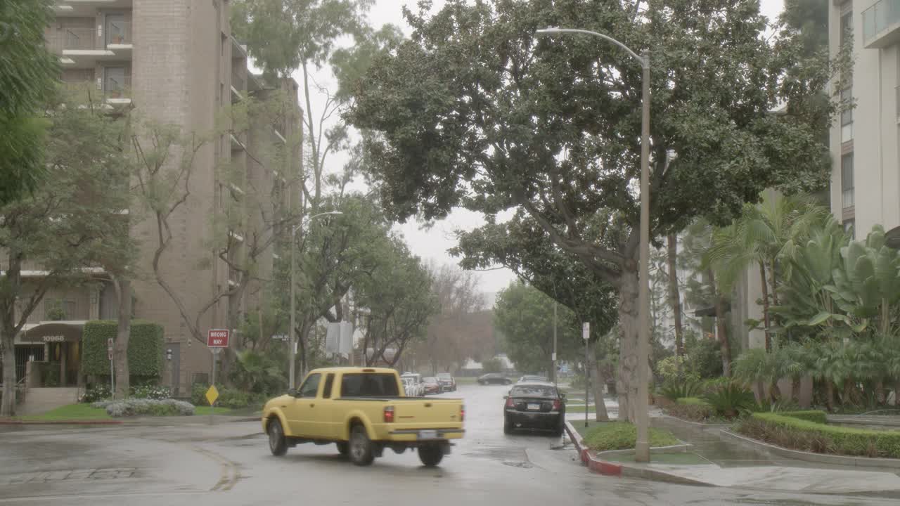 雨中城市街道的中等角度。可见多层公寓楼。汽车在城市街道上驶过。行人撑着伞走在人行道上。视频素材