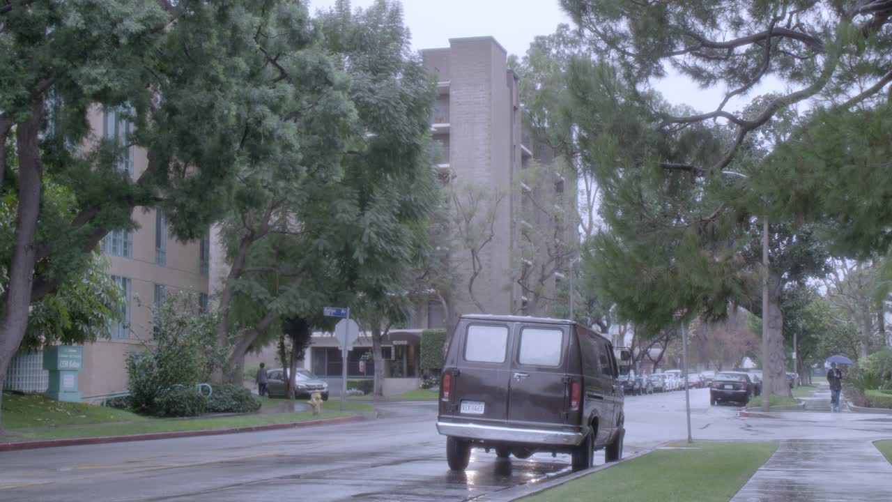 广角的城市街道与住宅小区。树木清晰可见。人行道上可见拿着雨伞的行人。汽车在雨中行驶在城市街道上。视频素材