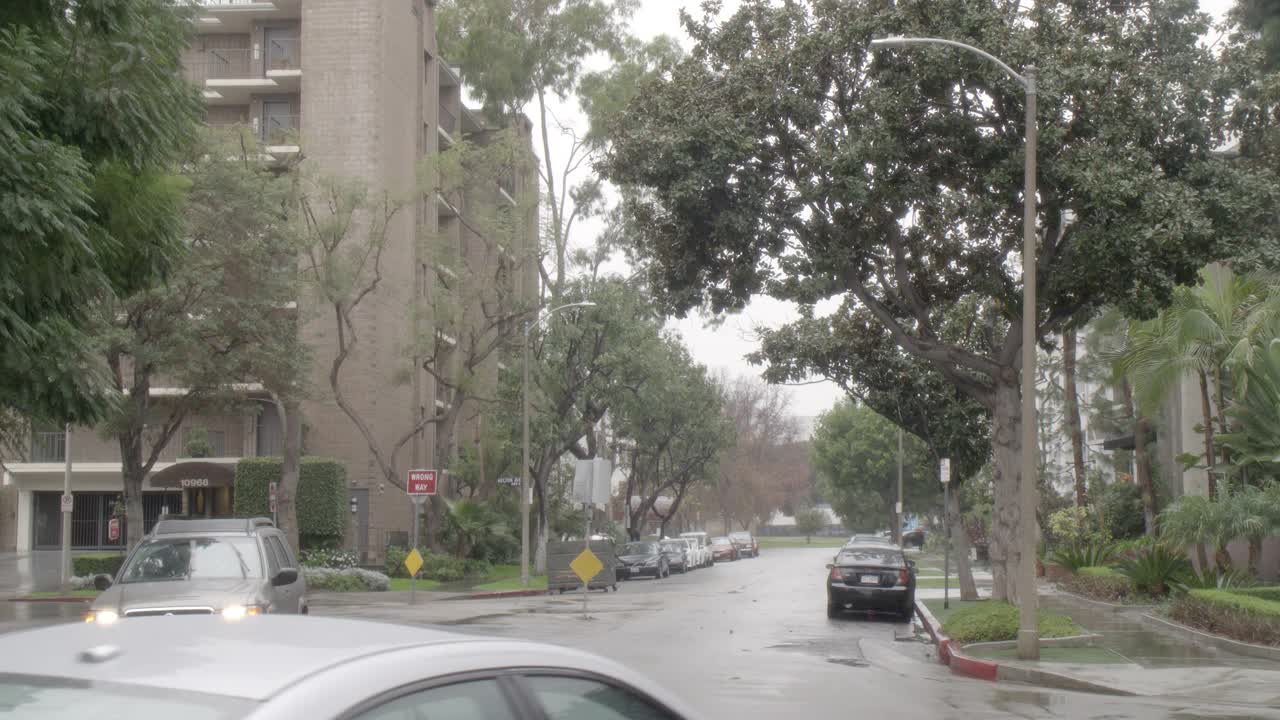 雨中城市街道的中等角度。可见多层公寓楼。汽车在城市街道上驶过。行人撑着伞走在人行道上。视频素材