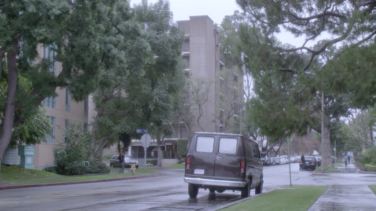 广角的城市街道与住宅小区。树木清晰可见。人行道上可见拿着雨伞的行人。汽车在雨中行驶在城市街道上。视频素材