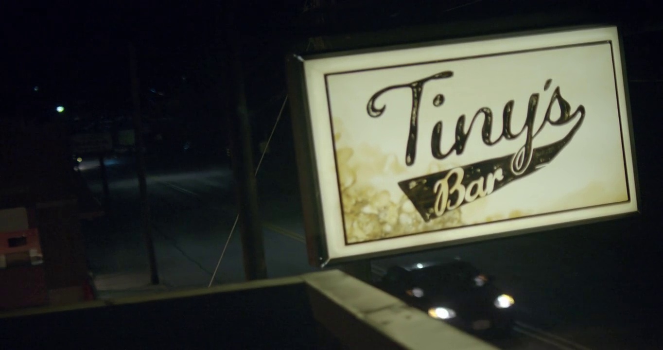 建筑物屋顶“tiny’s bar”标志的闭合角度。在bg的街道上可以看到汽车行驶。视频素材