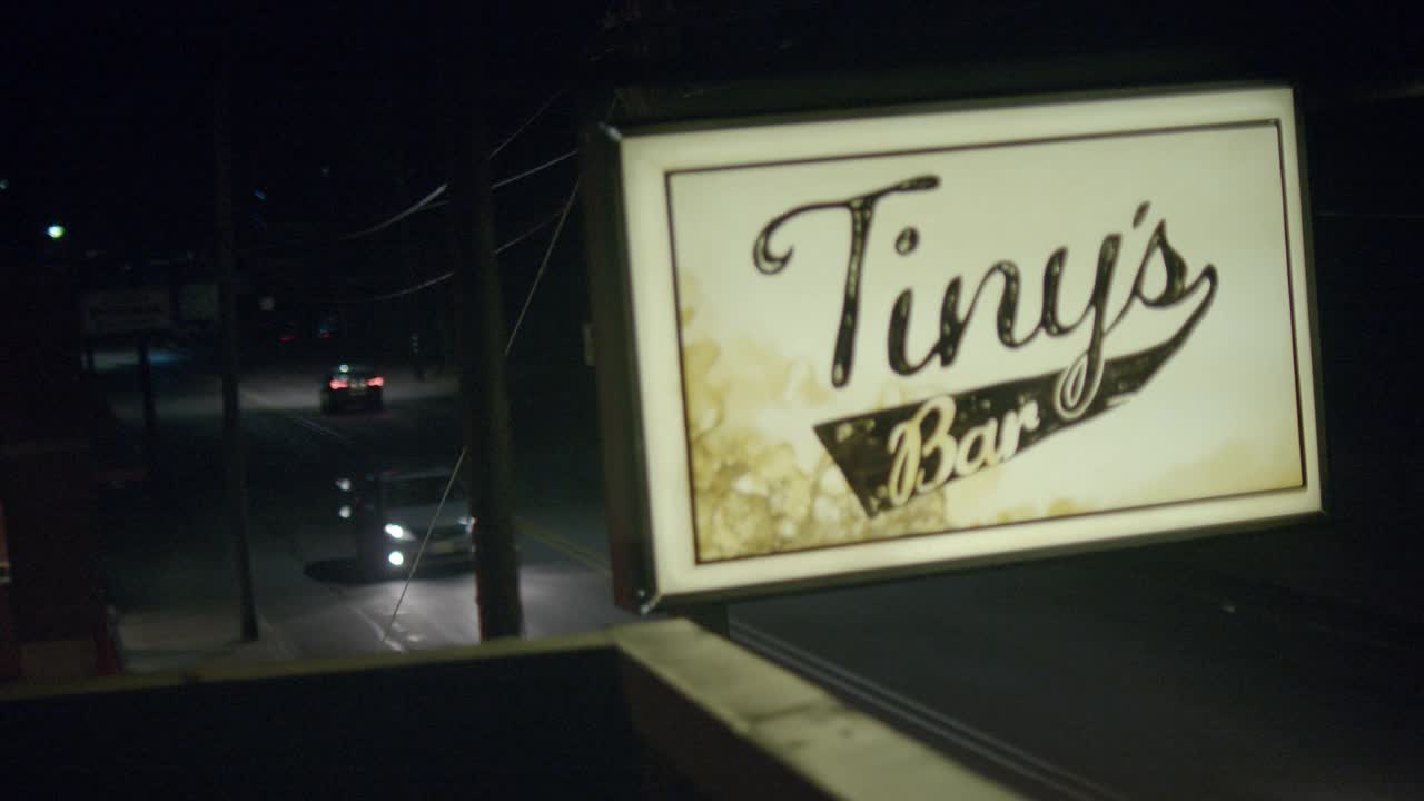 建筑物屋顶“tiny’s bar”标志的闭合角度。在bg的街道上可以看到汽车行驶。视频素材