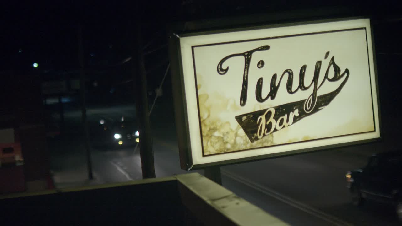 建筑物屋顶“tiny’s bar”标志的闭合角度。在bg的街道上可以看到汽车行驶。视频素材