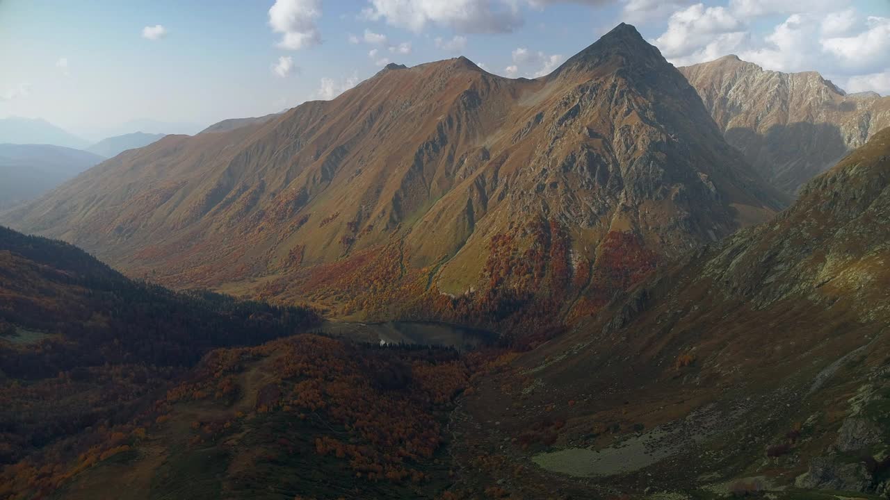 山谷中有一个清澈的高山湖泊，周围是秋天的森林。山谷中橙色、红色和黄色的森林。雄蜂飞过五彩缤纷的森林。非常美丽的山脉全景鸟瞰图视频素材