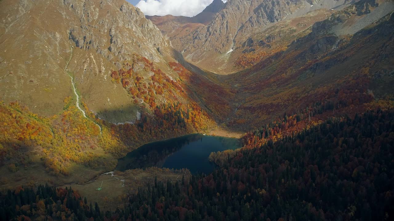 山谷中有一个清澈的高山湖泊，周围是秋天的森林。山谷中橙色、红色和黄色的森林。雄蜂飞过五彩缤纷的森林。非常美丽的山脉全景鸟瞰图视频素材