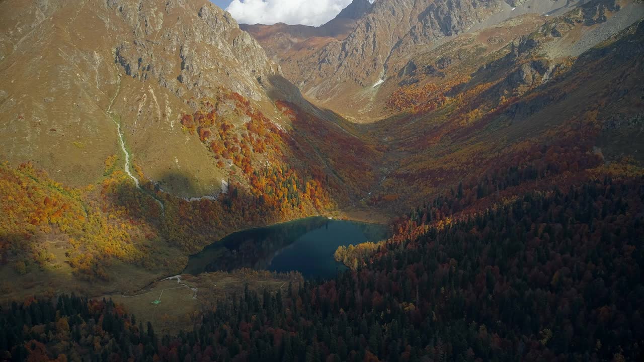 山谷中有一个清澈的高山湖泊，周围是秋天的森林。山谷中橙色、红色和黄色的森林。雄蜂飞过五彩缤纷的森林。非常美丽的山脉全景鸟瞰图视频素材